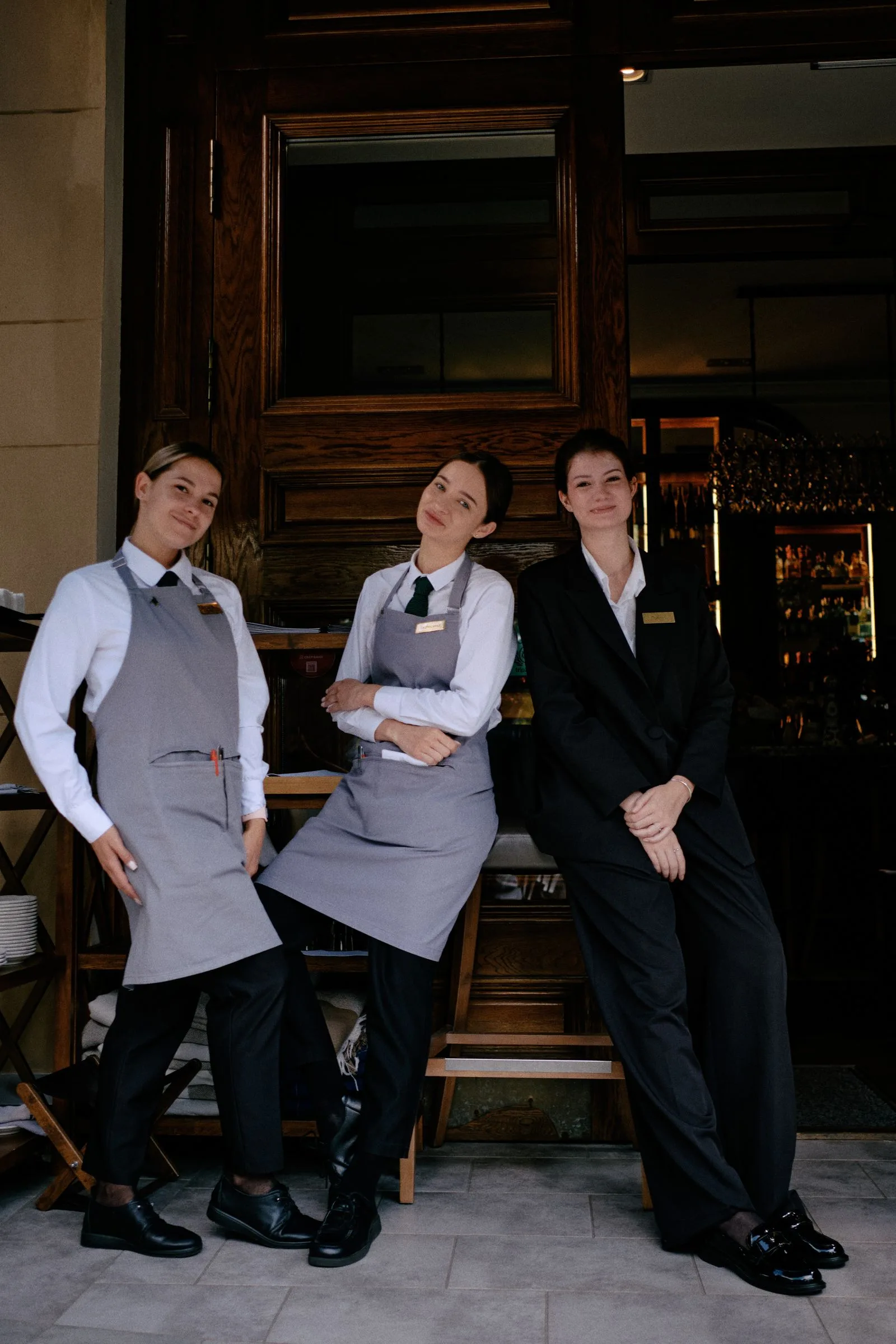 Restaurant staff in aprons and formalwear posing outside their restaurant