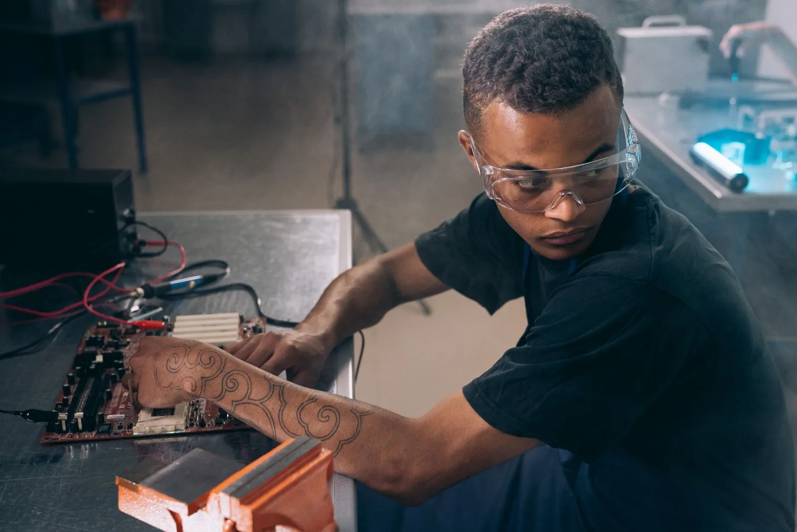 A technician wearing safety goggles working at an electronics workshop table