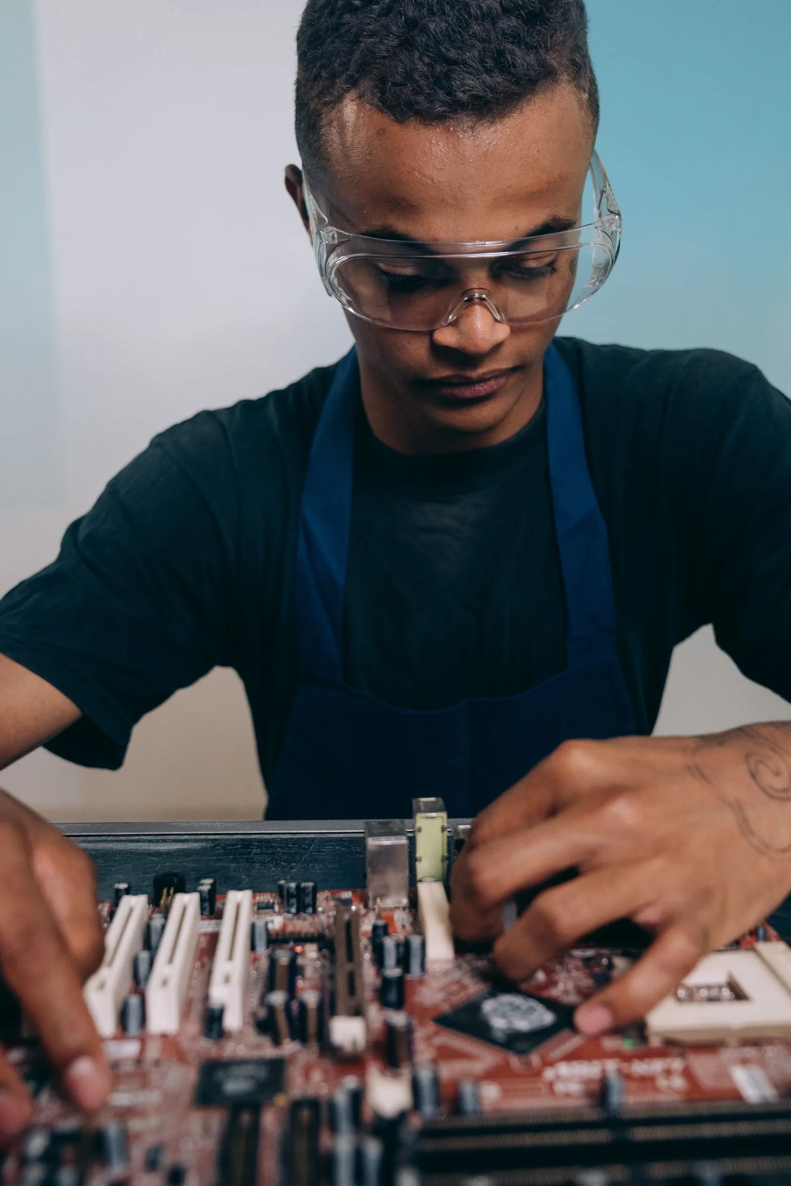 A technician in safety goggles and an apron working with electronics
