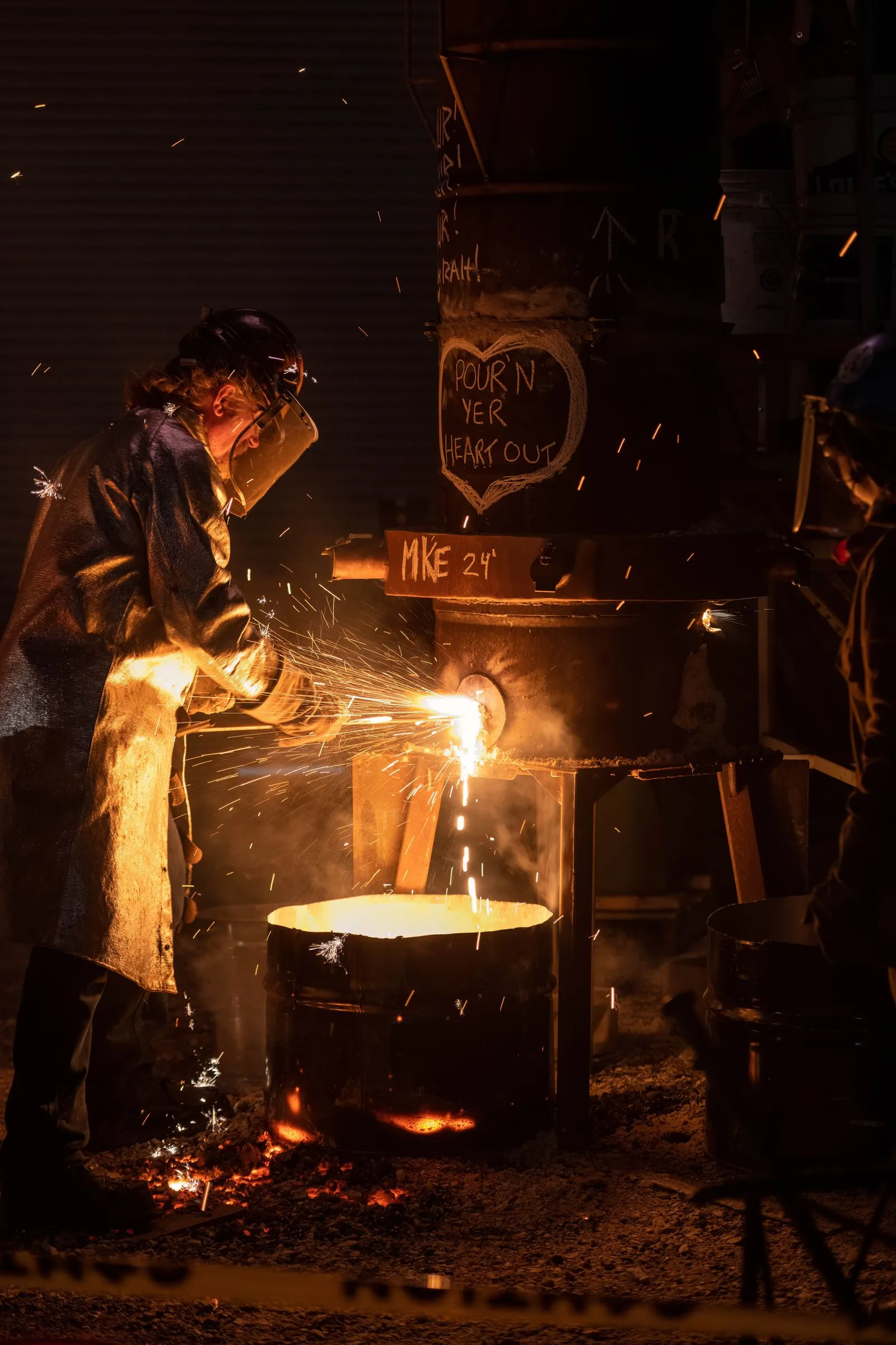 A foundry worker in protective gear pouring molten metal at an industrial facility
