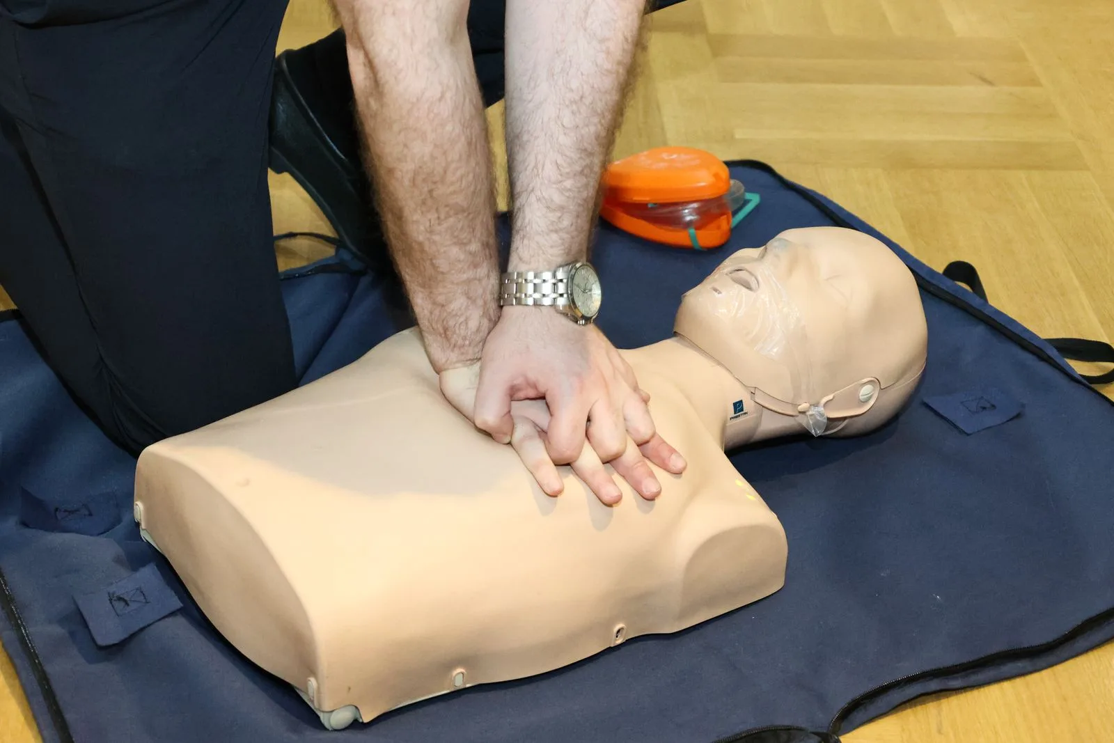 Two people practicing CPR technique on a training mannequin indoors